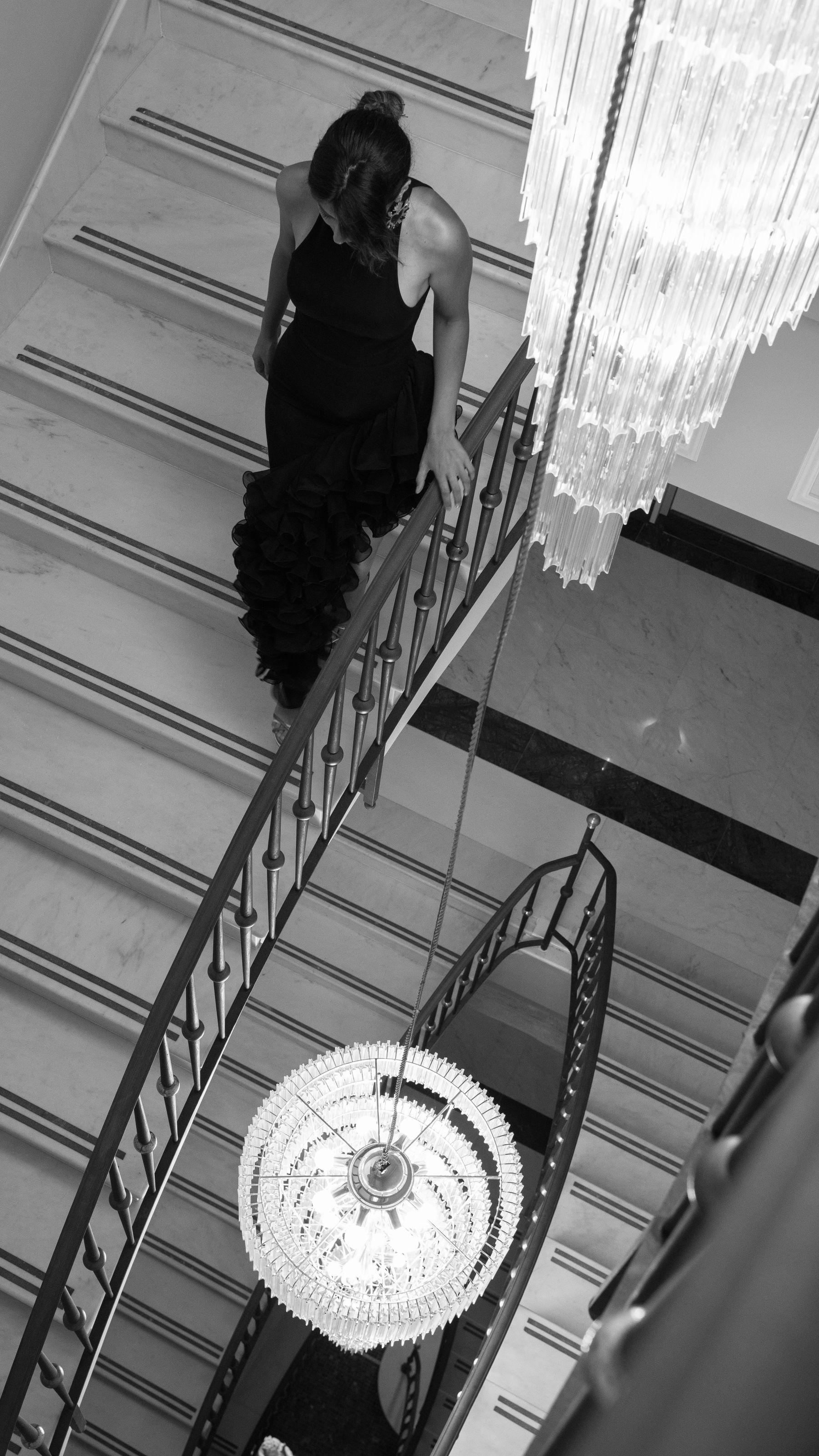 Femme en robe descendant un escalier de marbre sous un lustre